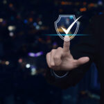 Businessman pressing security shield with check mark icon over blur colorful night light city tower and skyscraper.