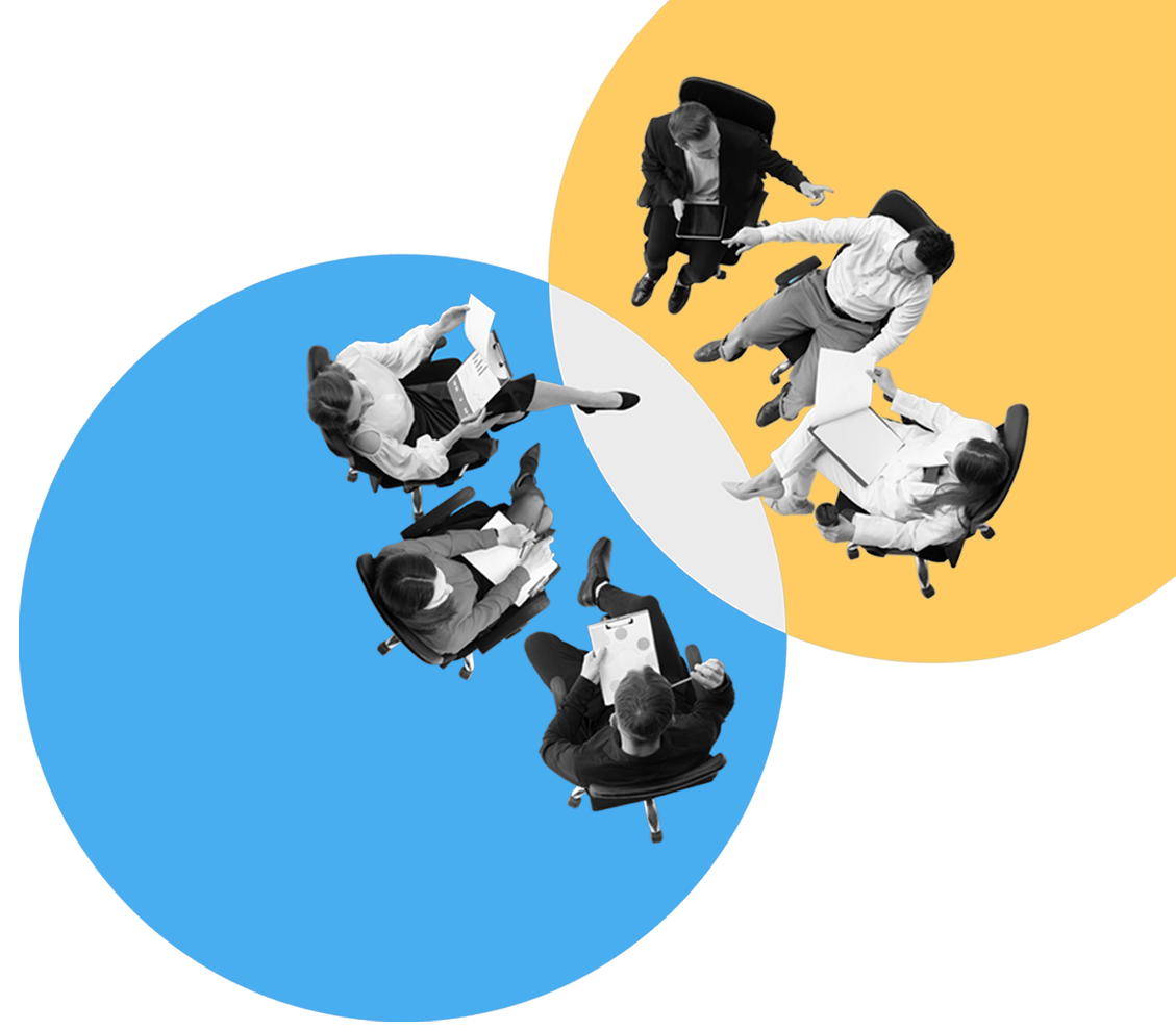 Header-Image-1 Aerial view of a diverse team collaborating around circular blue and yellow shapes, seen from above around a conference table setup.