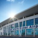 Exterior of Princess Juliana International Airport terminal with large glass windows and white angled columns, sun glare at top left. (informative)
